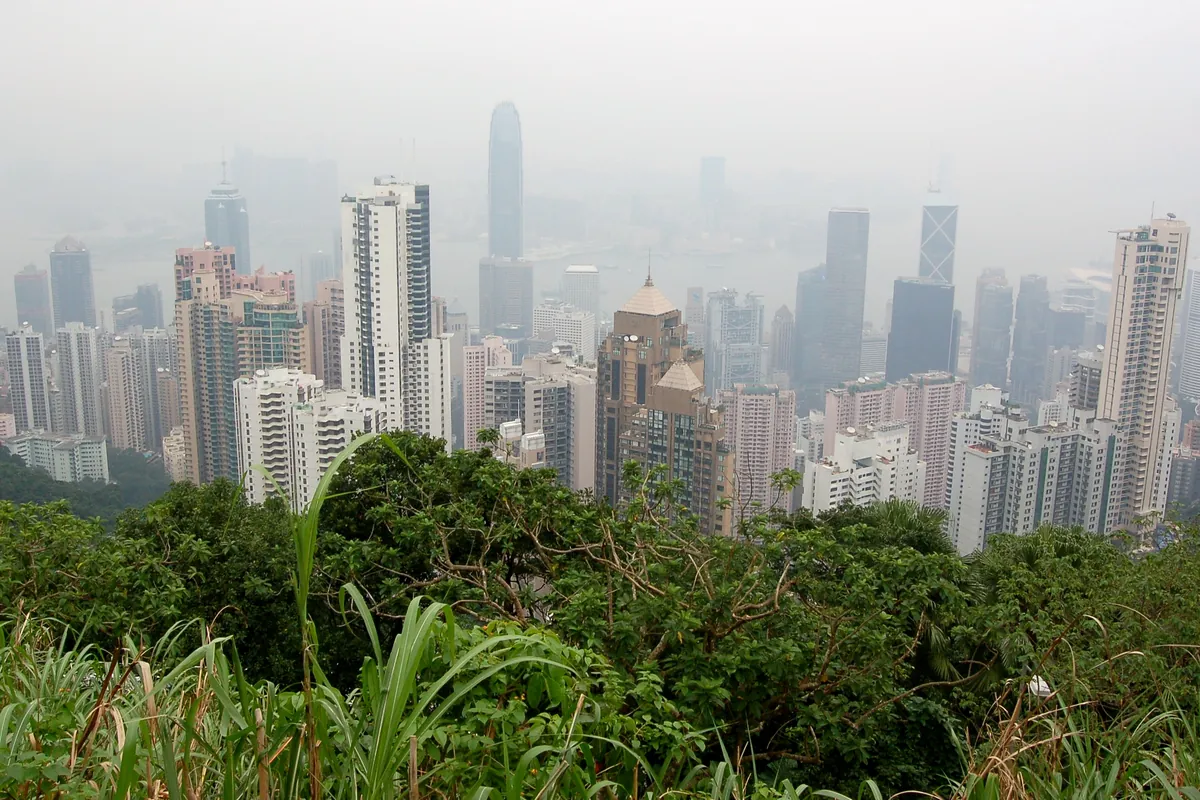 Hongkongské mrakodrapy mizející v bledém oparu nad zeleným svahem, pohled z Peak Tower