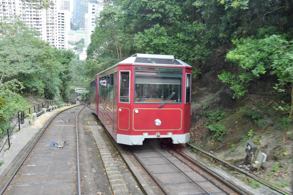 Starší generace červeného vozu Peak Tram přijíždí k výhybně na zalesněném svahu Victoria Peak