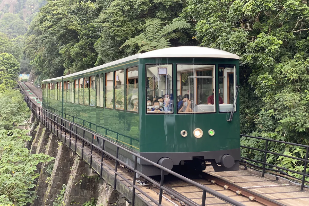 En grøn Peak Tram-vogn på en stenviadukt over en skovklædt skråning